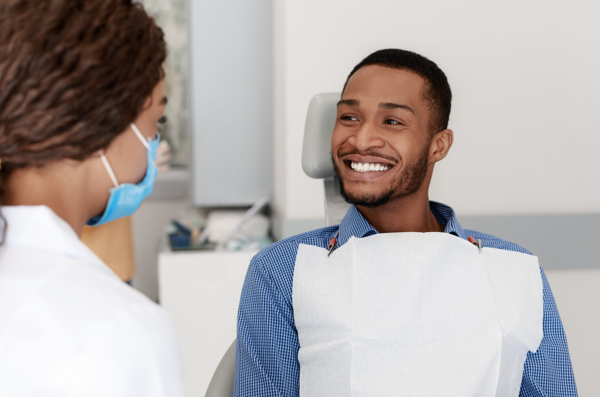 Young african man smiling to his female dentist doctor while having treatment at modern dental clinic