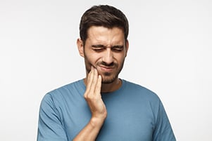 Young man wincing in pain and holding his jaw, needing wisdom teeth removal at Dens Dental Studio in Chicago, IL.