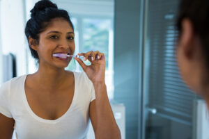 Woman brushing teeth in bathroom at Dens Dental Studio in Chicago, IL.