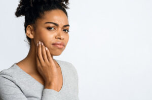 Young woman in pain and holding her jaw due to a cavity, needing treatment from Dens Dental Studio in Chicago, IL.