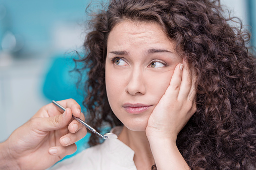 Young woman holding her cheek in pain during emergency appointment at Dens Dental Studio in Uptown Chicago, IL.