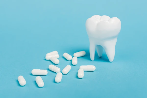 3D-printed tooth sitting on a blue background next a scattered number of plain, white pills illustrated by Dens Dental Studio in Uptown Chicago, IL.