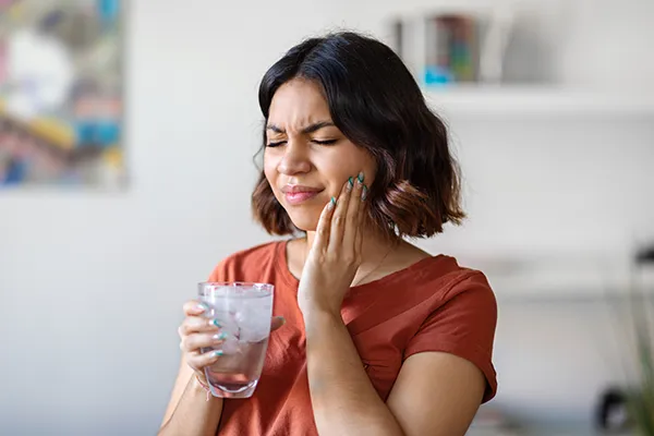 Young woman in pain and holding her cheek, in need of cracked tooth treatment at Dens Dental Studio in Uptown Chicago, IL