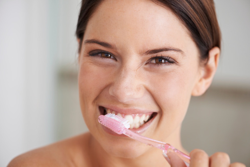 A gorgeous young brunette brushing her teeth after cracked tooth repair at Dens Dental Studio in Uptown Chicago, IL.