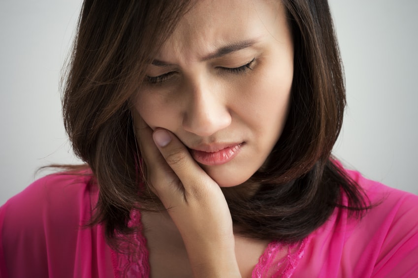 Young woman holding her jaw in pain, needing treatment from at Dens Dental Studio in Uptown Chicago, IL.