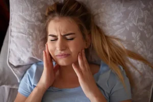 Woman with sensitive teeth, holding her jaw in pain, needing repair from Dens Dental Studio in Uptown Chicago, IL